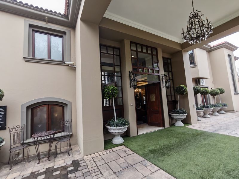 Grand covered entrance featuring a timber front door, large glass windows, elegant wrought iron lighting, and a well-maintained paved patio area.