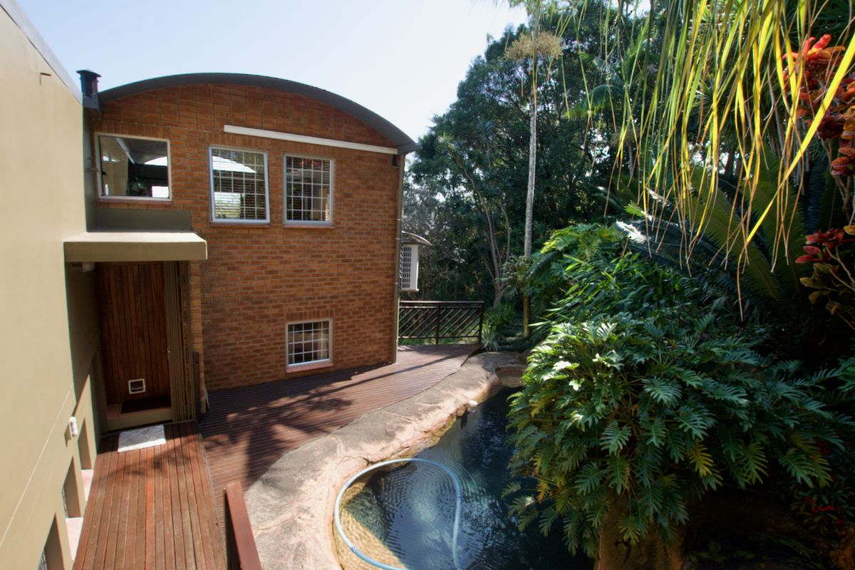Rear exterior view of the townhouse featuring a brick facade, timber decking, and a swimming pool surrounded by lush garden landscaping.