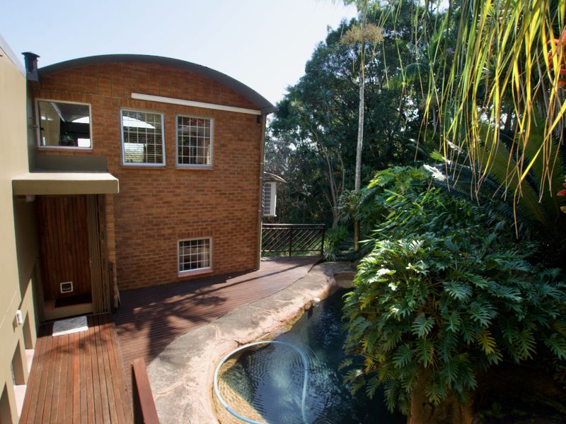 Rear exterior view of the townhouse featuring a brick facade, timber decking, and a swimming pool surrounded by lush garden landscaping.