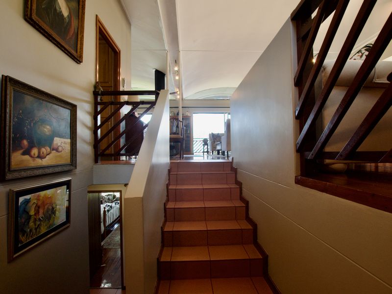 A split-level hallway featuring a tiled staircase with timber balustrades leading towards an open-plan living area with a vaulted ceiling.