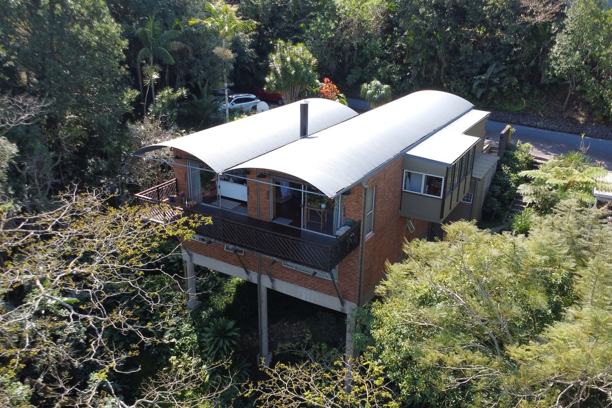 Aerial view of a unique townhouse featuring a curved metal roof, brick exterior, and elevated structure nestled within a lush, wooded environment.