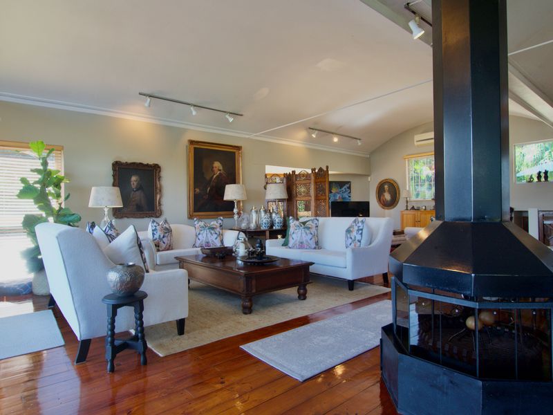 Spacious living room featuring polished hardwood floors, a prominent black freestanding fireplace, and track lighting under a vaulted ceiling.