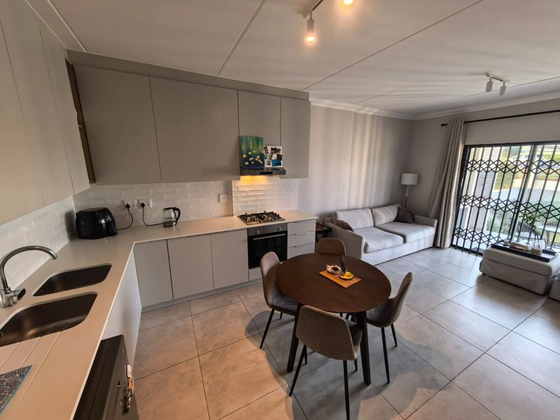 Modern open-plan apartment featuring a sleek kitchen with quartz countertops, subway tile backsplash, gas hob, and tiled flooring leading to a secure patio entrance.