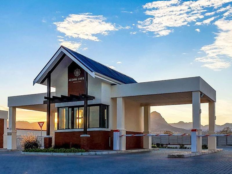 The main entrance and security gatehouse of the Acorn Creek estate, featuring a modern architectural design with paved access and boom gate infrastructure.