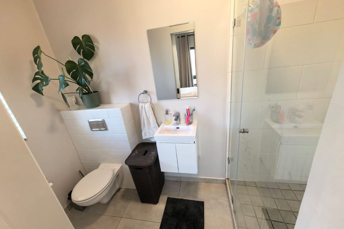 A modern bathroom featuring a wall-hung toilet with a concealed cistern, a compact vanity basin, and a glass-enclosed shower with tiled finishes.