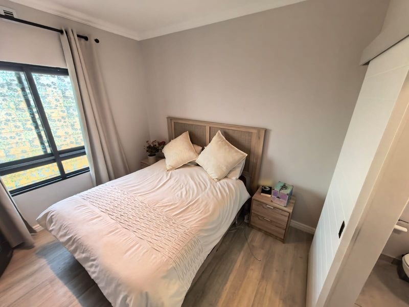 A well-maintained bedroom featuring light-toned laminate flooring, neutral wall finishes, and a large window providing natural light.