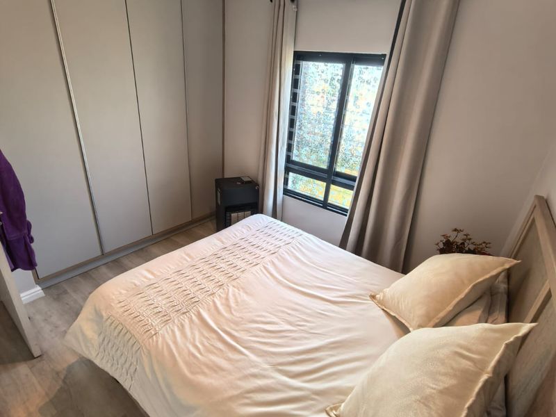 A well-maintained bedroom featuring modern laminate flooring, built-in cupboards, and neutral finishes, offering a clean and comfortable living space.