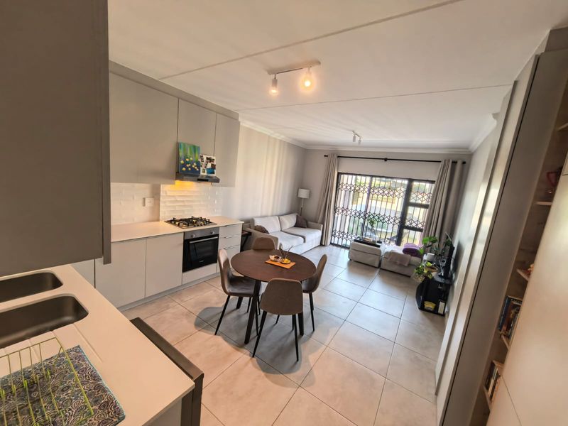 Modern open-plan living area featuring a contemporary kitchen with built-in appliances, tiled flooring, and direct access to a balcony through a sliding security door.