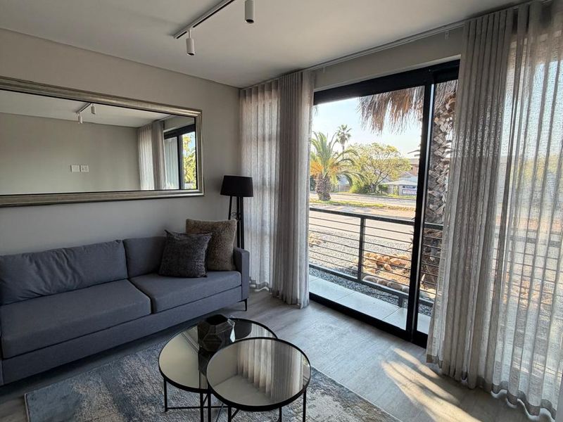 A bright living room featuring modern track lighting, laminate flooring, and large sliding glass doors that open to an outdoor area.