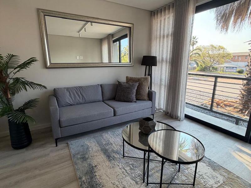 A bright living room featuring modern track lighting, laminate flooring, and a large sliding glass door providing access to a balcony.
