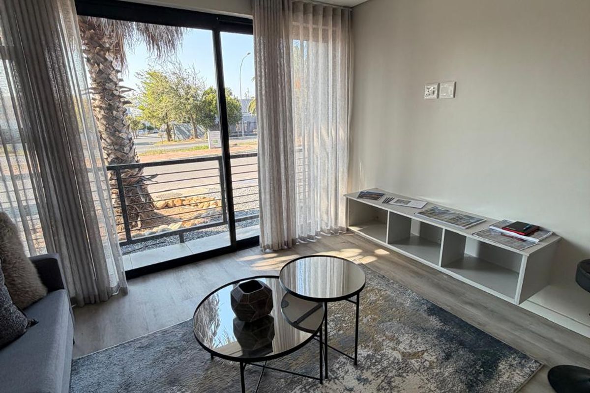 A bright living room featuring modern track lighting, laminate flooring, and a large sliding glass door that opens to an outdoor area.