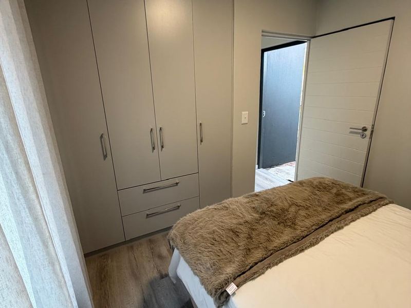 A well-maintained bedroom featuring modern built-in cupboards, light-toned laminate flooring, and a neutral color palette.