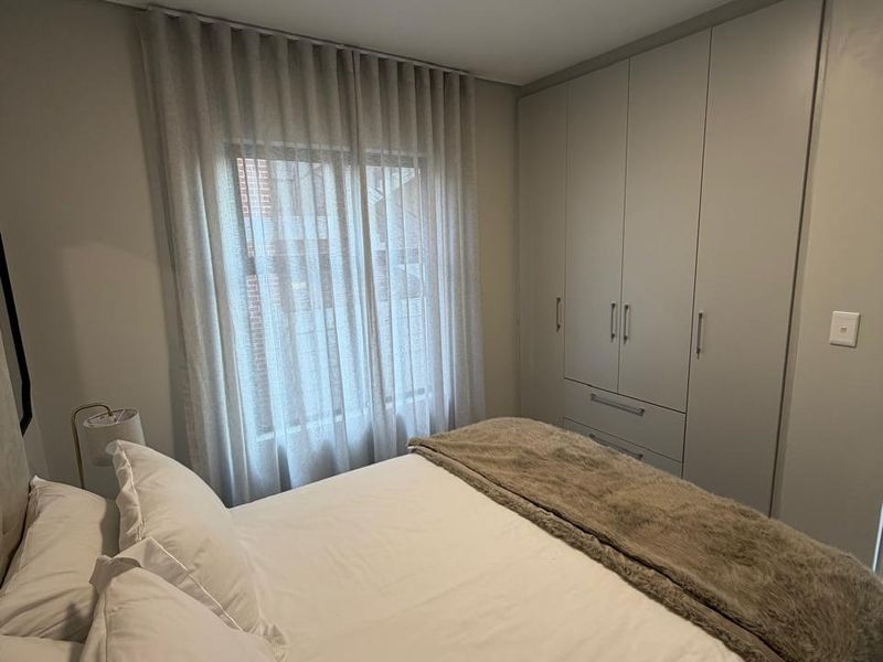 A well-maintained bedroom featuring neutral tones, a built-in wardrobe with ample storage, and soft window treatments.