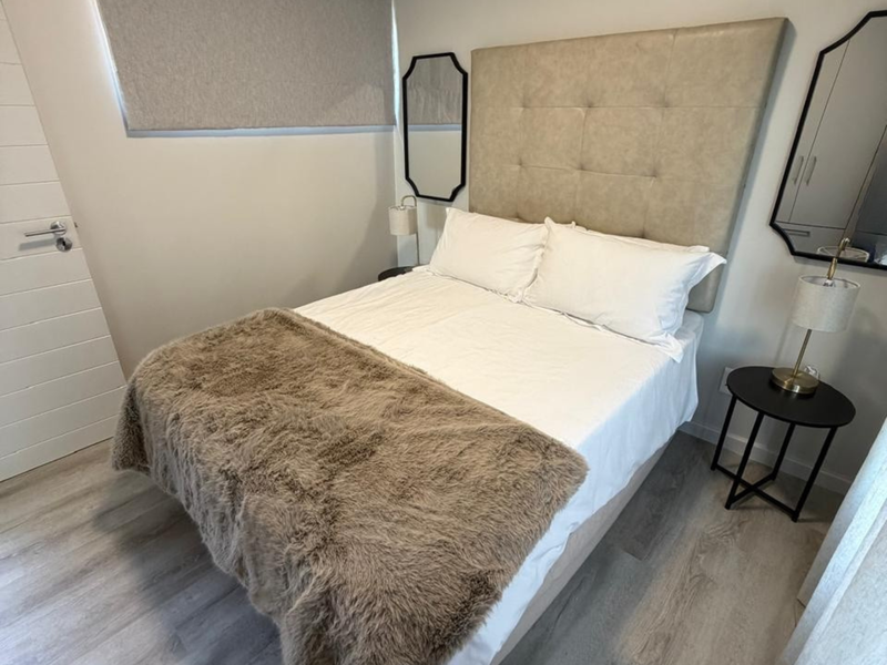 A well-maintained bedroom featuring light-toned laminate flooring, neutral wall finishes, and a modern roller blind for privacy.
