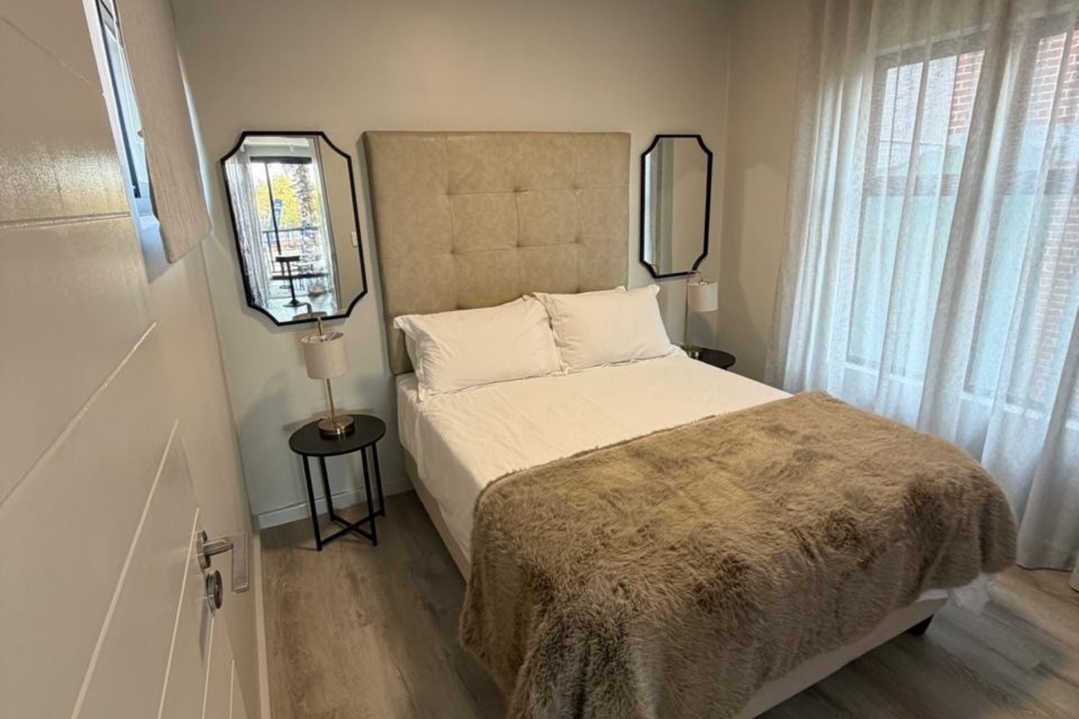 A well-maintained bedroom featuring light-toned laminate flooring, neutral wall finishes, and large windows with fitted curtain tracks.