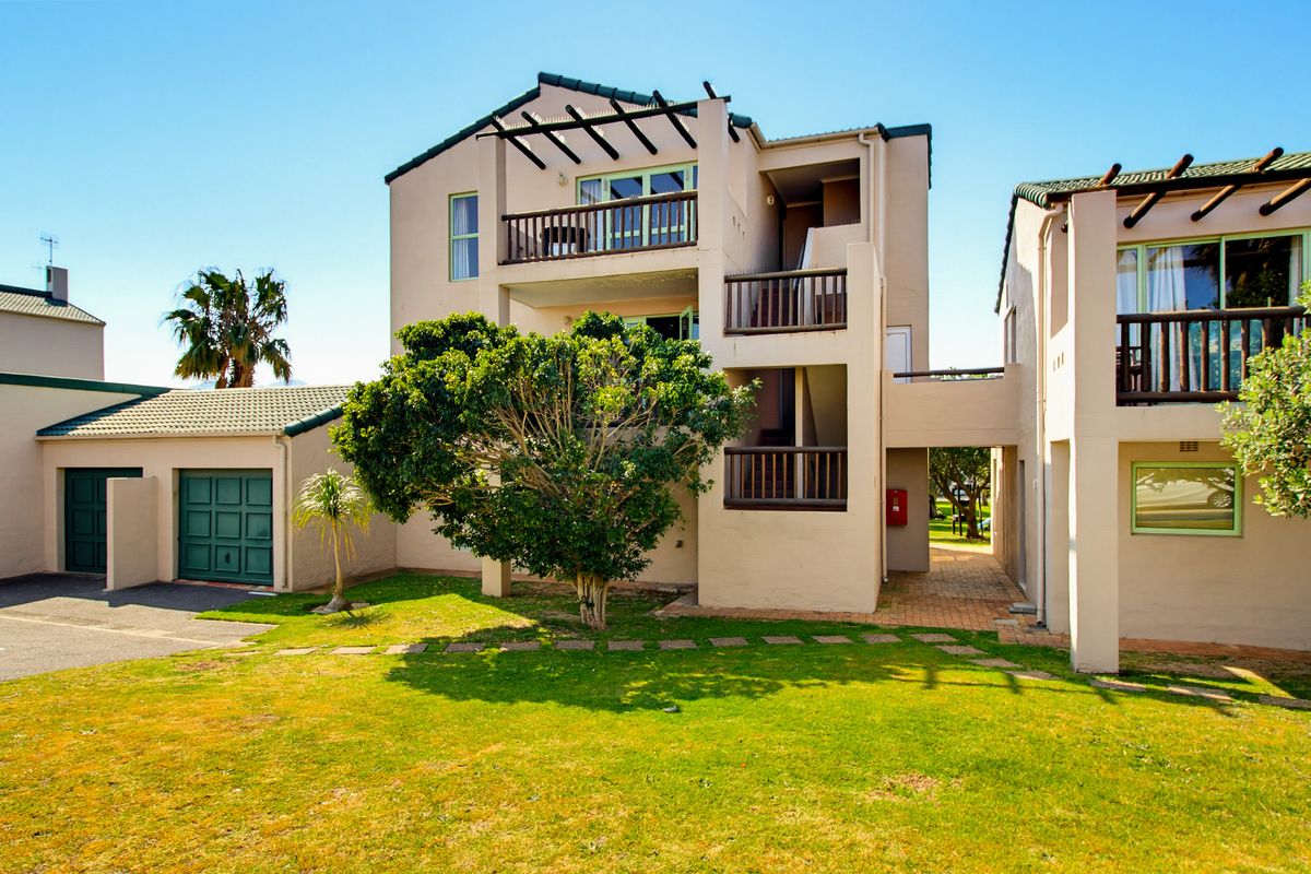 Rear view of a multi-story apartment complex featuring balconies, a paved walkway, and an attached garage with a landscaped garden area.