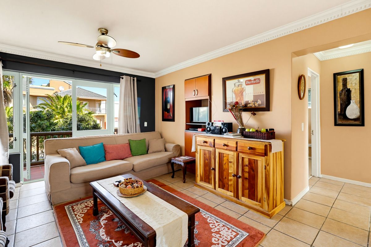 A comfortable living room featuring tiled flooring, crown molding, a ceiling fan, and a sliding glass door providing access to an outdoor balcony.