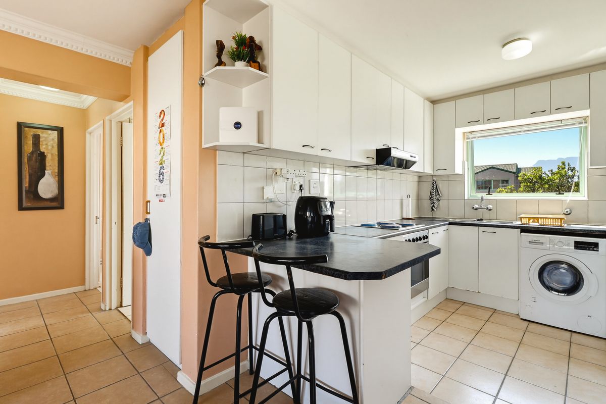 A functional kitchen featuring white cabinetry, tiled backsplash, integrated appliances, and a built-in breakfast bar with tiled flooring.