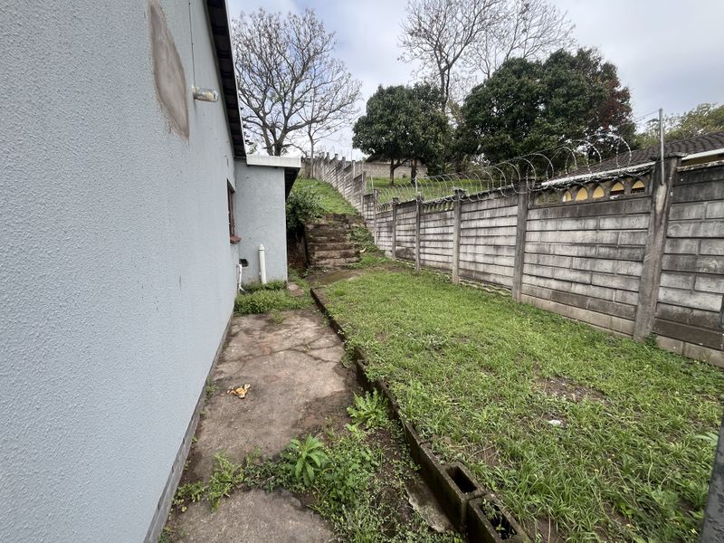 Rear exterior view showing a concrete pathway, boundary wall with security razor wire, and concrete stairs leading to an elevated garden area.