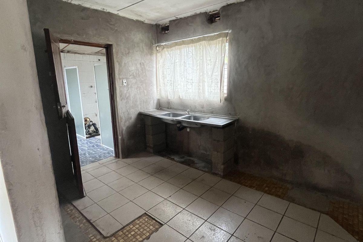 An unfinished kitchen space featuring a double sink, tiled flooring, and exposed wall surfaces, requiring significant renovation and completion.