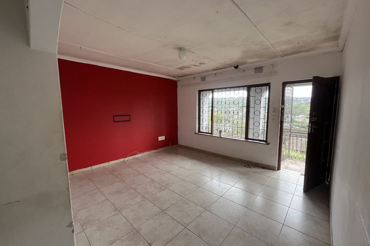 An empty living room featuring tiled floors, security bars on windows, and a security gate, requiring ceiling and wall repairs.