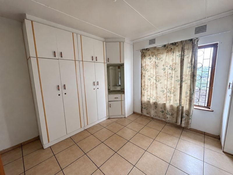 A bedroom featuring tiled flooring and extensive built-in cupboards with an integrated vanity unit, offering ample storage space.
