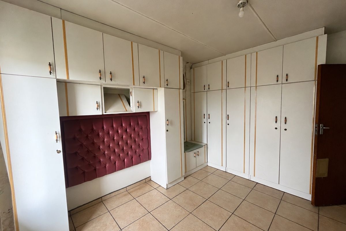 A bedroom featuring extensive built-in cabinetry with integrated headboard and neutral tiled flooring, offering ample storage space.