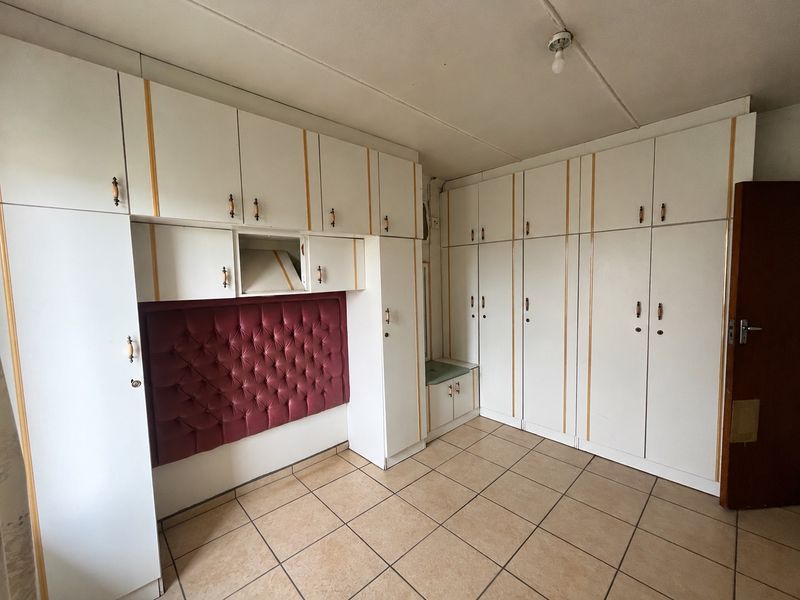 A bedroom featuring extensive built-in cabinetry with integrated headboard and neutral tiled flooring, offering ample storage space.
