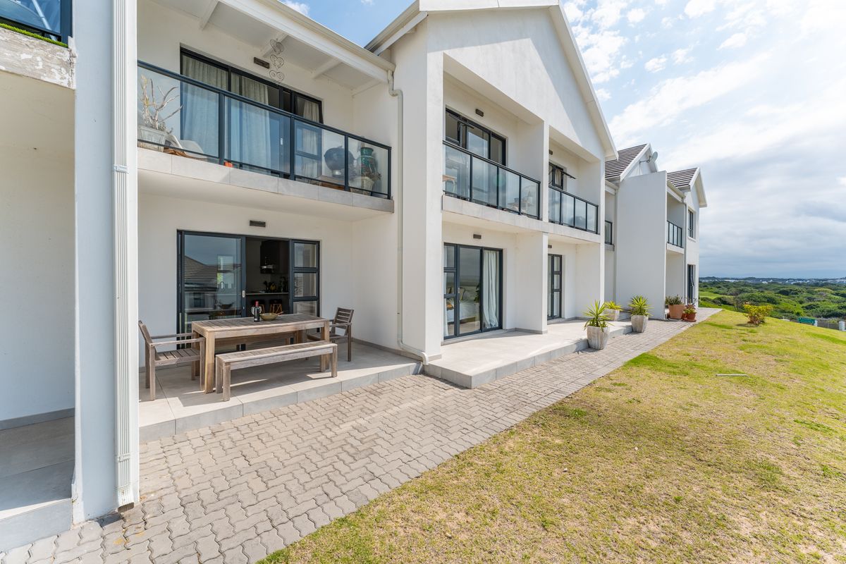 Rear view of the apartment complex featuring ground floor paved patios, upper level balconies with glass balustrades, and sliding door access.