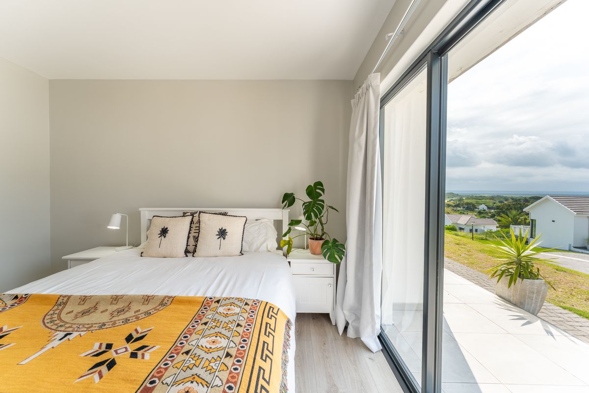 Bright bedroom featuring laminate flooring and large sliding glass doors that provide direct access to an outdoor patio area with scenic views.