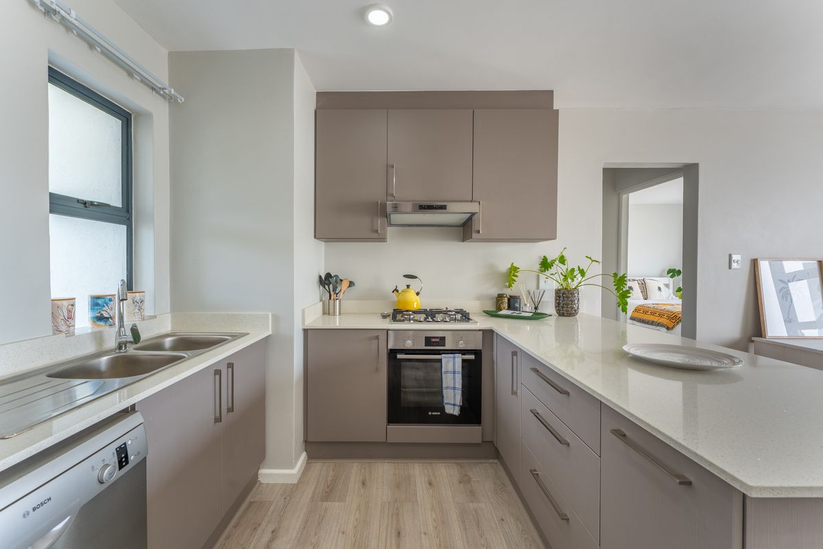 Modern kitchen featuring sleek taupe cabinetry, quartz countertops, integrated gas hob, built-in oven, and a double bowl sink with light wood-look flooring.