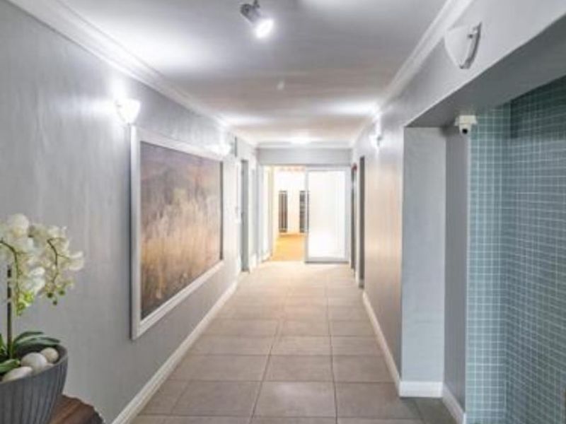 A well-lit, spacious apartment hallway featuring neutral tiled flooring, modern wall sconces, and a decorative mosaic tile accent wall.