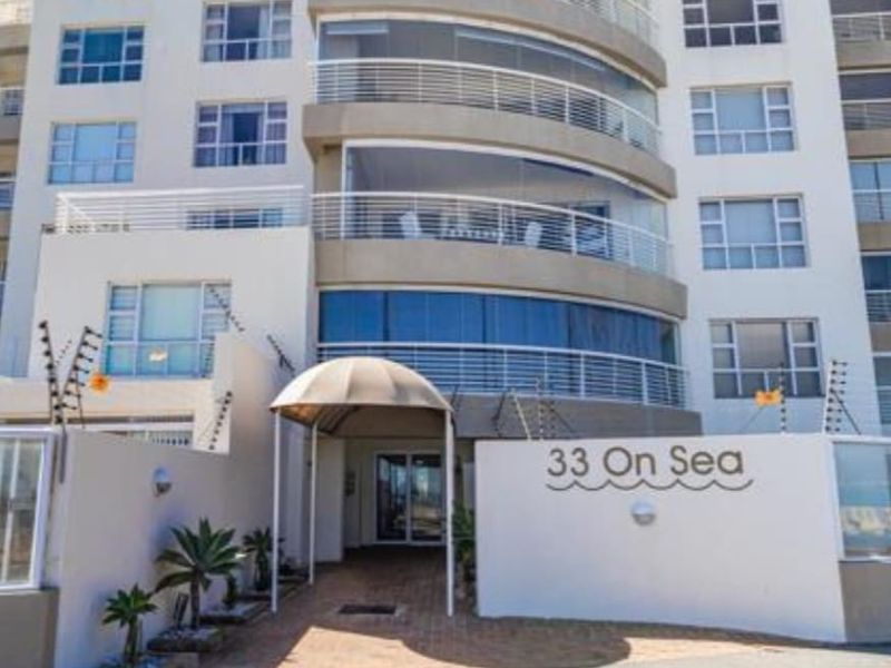 Front entrance view of 33 On Sea apartment building, featuring a paved driveway, modern glass balustrades, and secure electric fencing.