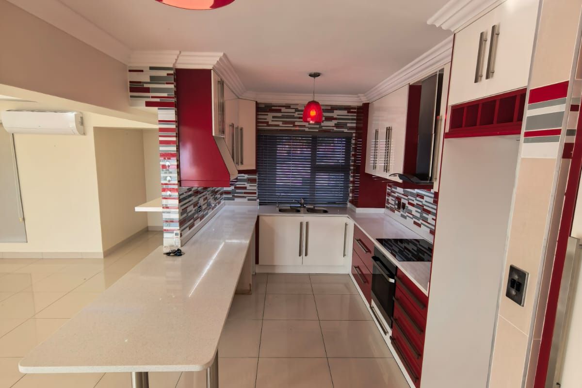 Modern kitchen featuring white and red cabinetry, stone countertops, a breakfast bar, built-in oven, hob, and tiled flooring in an open-plan layout.