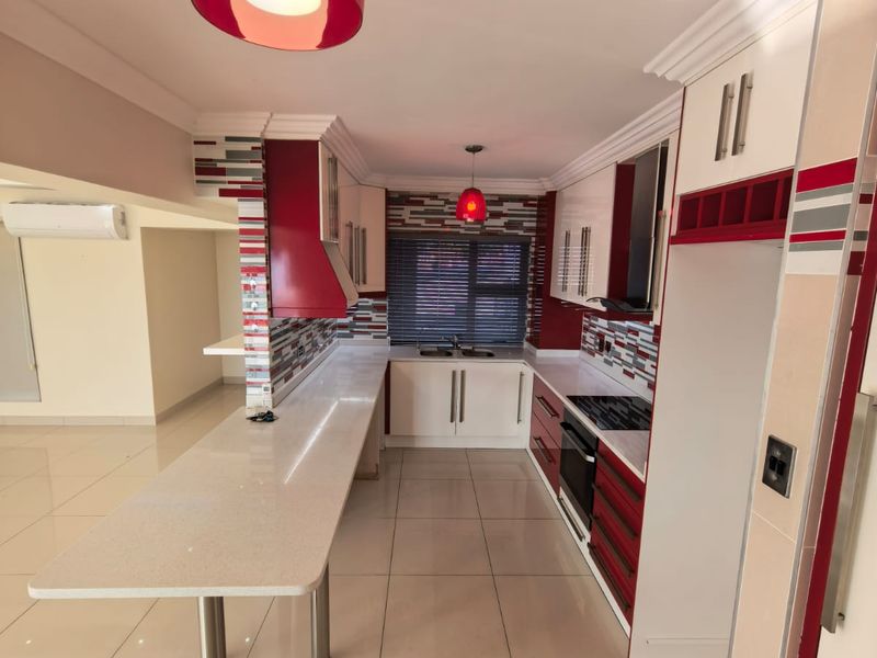 Modern kitchen featuring white and red cabinetry, stone countertops, a breakfast bar, built-in oven, hob, and tiled flooring in an open-plan layout.