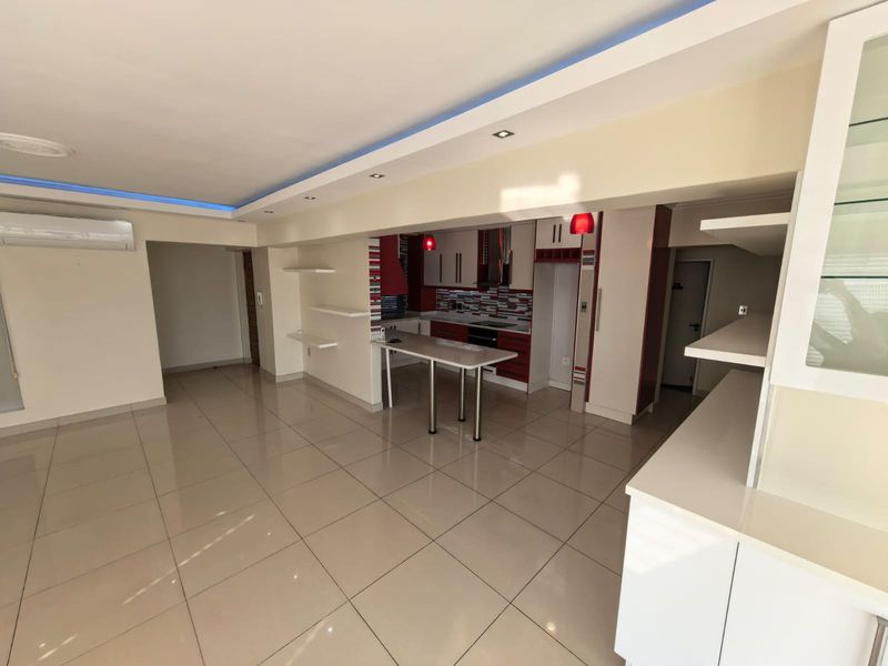 Spacious open-plan living and kitchen area featuring modern cabinetry, a breakfast island, tiled flooring, and integrated ceiling lighting.