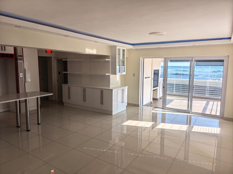 Spacious open-plan living area featuring polished tile floors, modern built-in cabinetry, and seamless access to a balcony with ocean views.