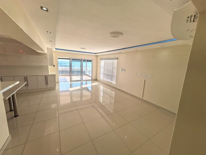 Spacious open-plan living area featuring polished porcelain tiles, modern recessed and cove lighting, and direct access to a balcony with ocean views.