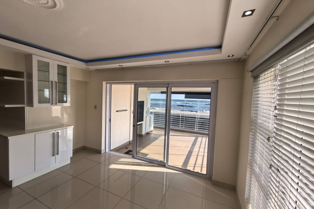 Bright living area featuring tiled floors, built-in cabinetry, and sliding glass doors opening onto a balcony with ocean views.