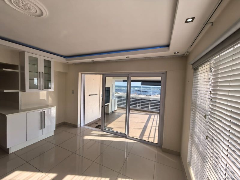Bright living area featuring tiled floors, built-in cabinetry, and sliding glass doors opening onto a balcony with ocean views.