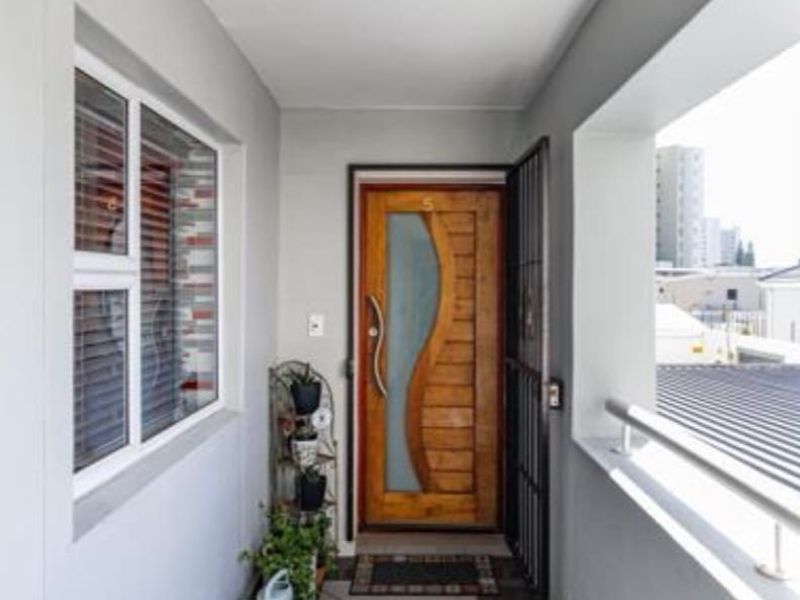 A well-maintained apartment entrance featuring a decorative wooden front door, security gate, and tiled flooring with a metal balcony railing.