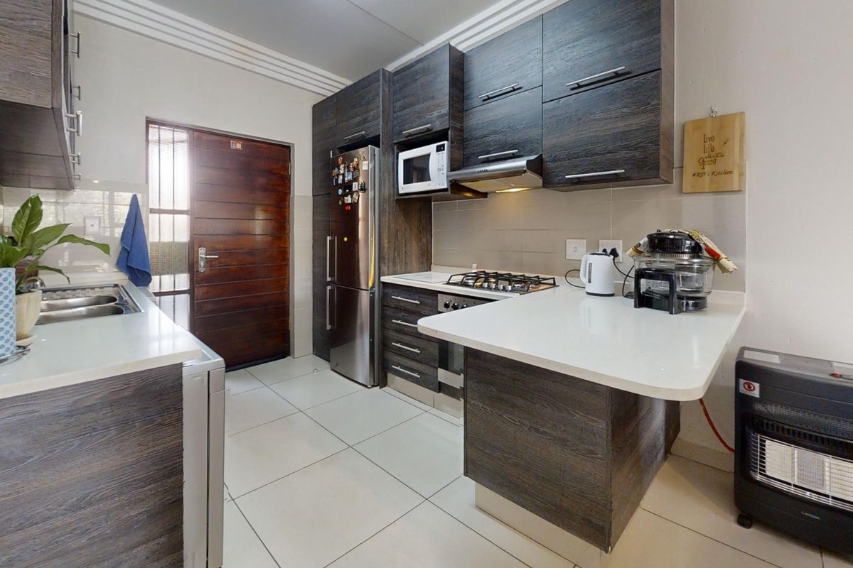 Modern kitchen featuring dark wood-grain cabinetry, stone countertops, gas hob, extractor fan, and built-in microwave with tiled flooring and direct exterior access.