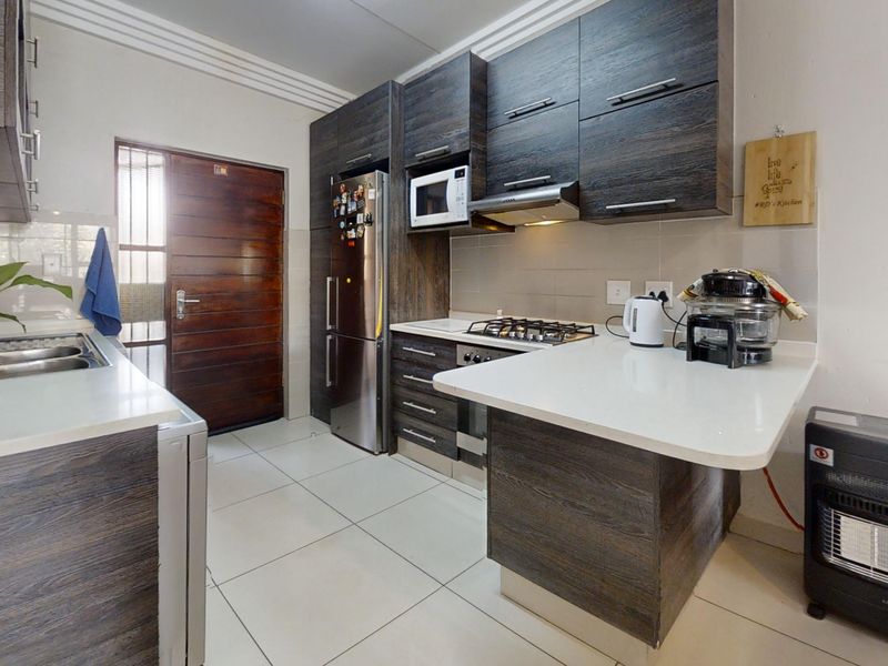 Modern kitchen featuring dark wood-grain cabinetry, stone countertops, gas hob, extractor fan, and built-in microwave with tiled flooring and direct exterior access.