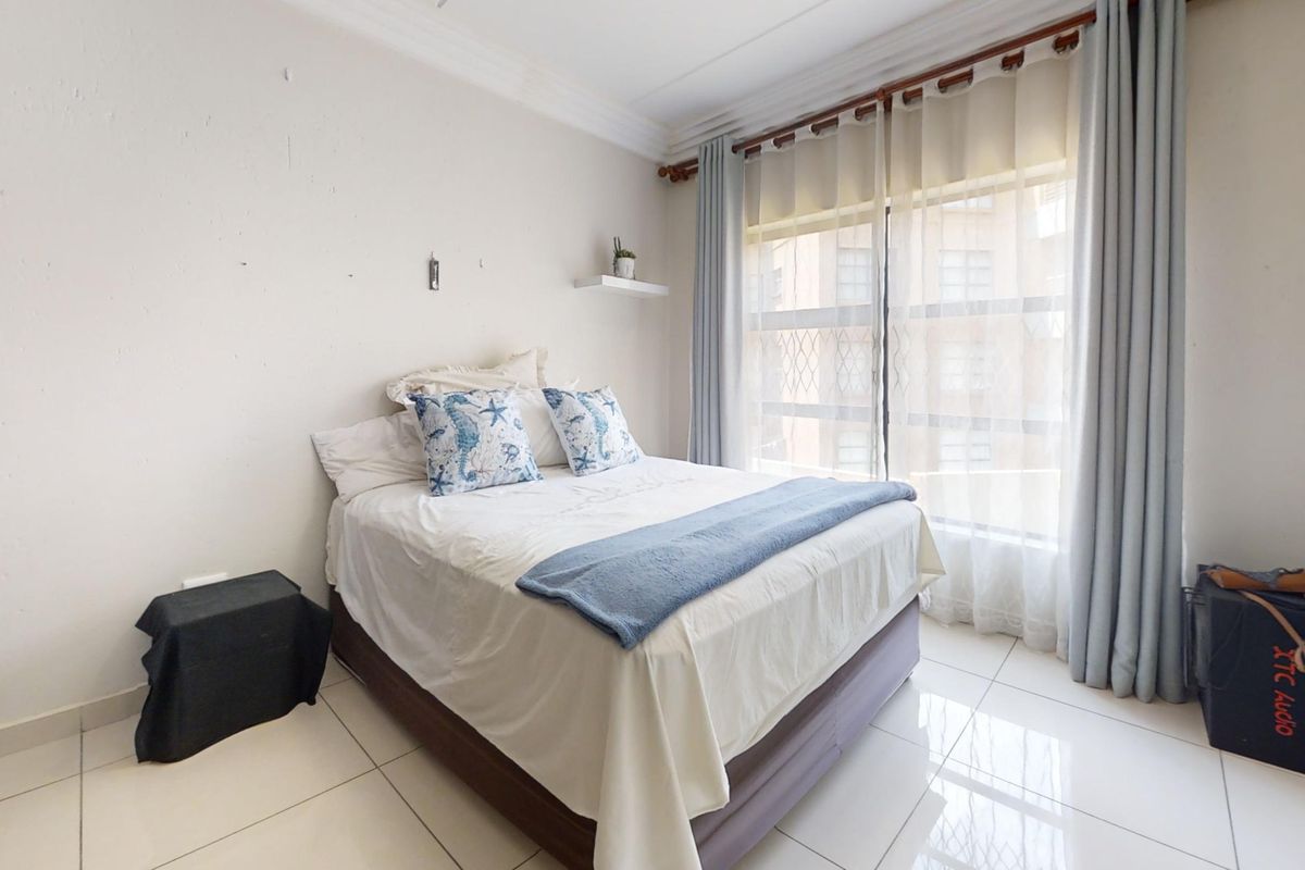 A bright bedroom featuring tiled flooring, built-in wardrobe storage, and large windows with security gates, offering a functional and well-lit living space.
