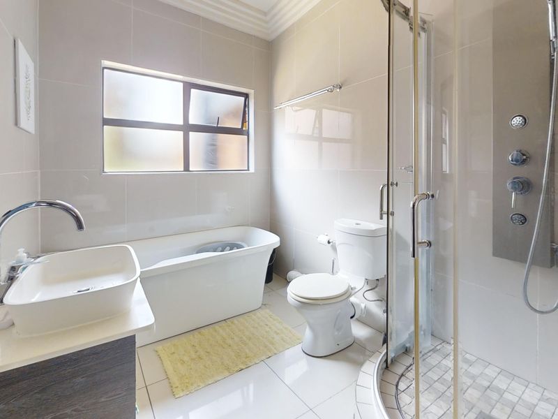 Modern bathroom featuring a freestanding bathtub, separate shower enclosure with body jets, vessel sink vanity, and neutral floor-to-ceiling tiling.