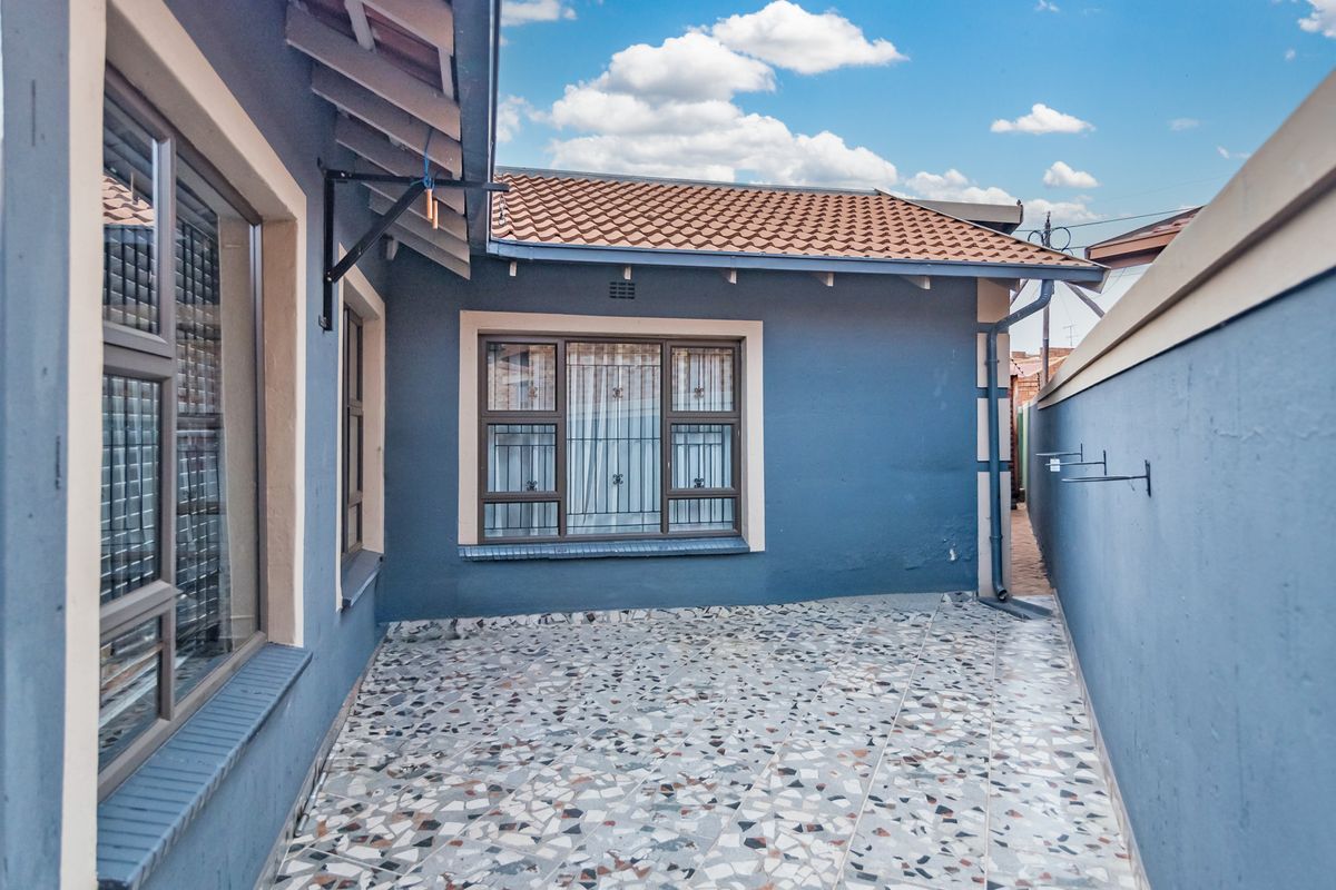 A well-maintained rear exterior area featuring terrazzo flooring, exposed rafters, and secure window treatments against a blue-painted facade.