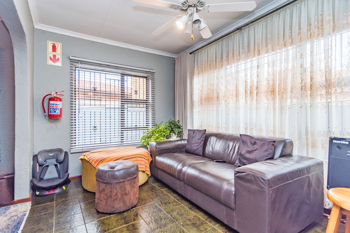 A living room featuring tiled flooring, a ceiling fan, and security bars on the windows.