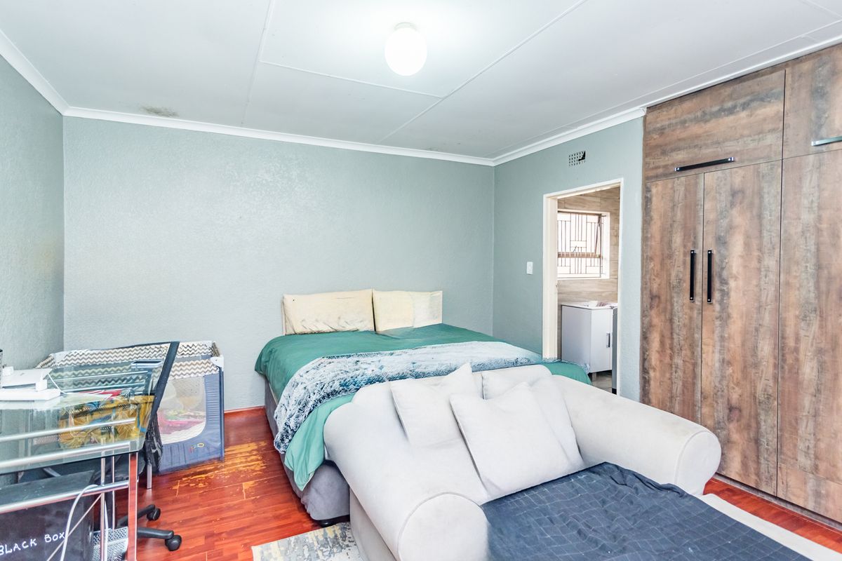 A bedroom featuring built-in wooden cupboards, laminate flooring, and a ceiling light fixture, with an adjacent en-suite bathroom visible.