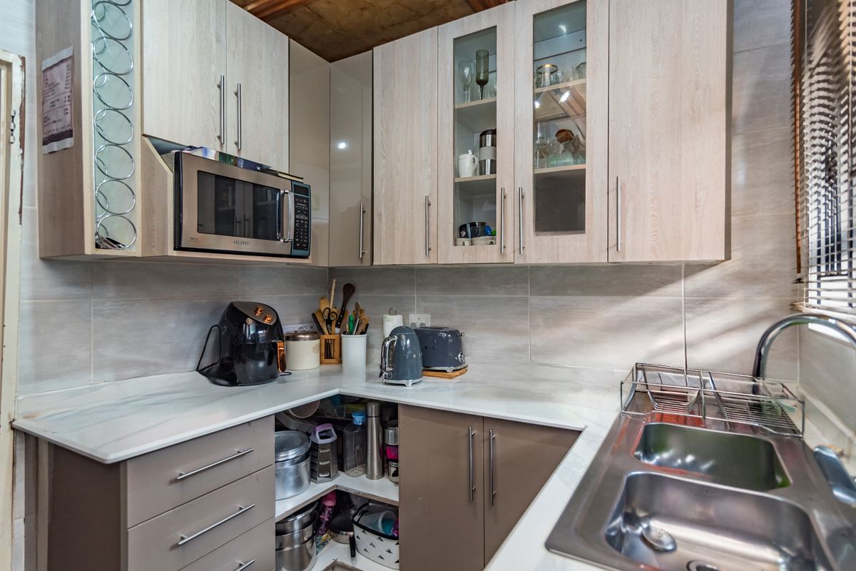 A functional kitchen featuring light wood-tone cabinetry, marble-effect countertops, a stainless steel double sink, and built-in microwave with tiled backsplash.
