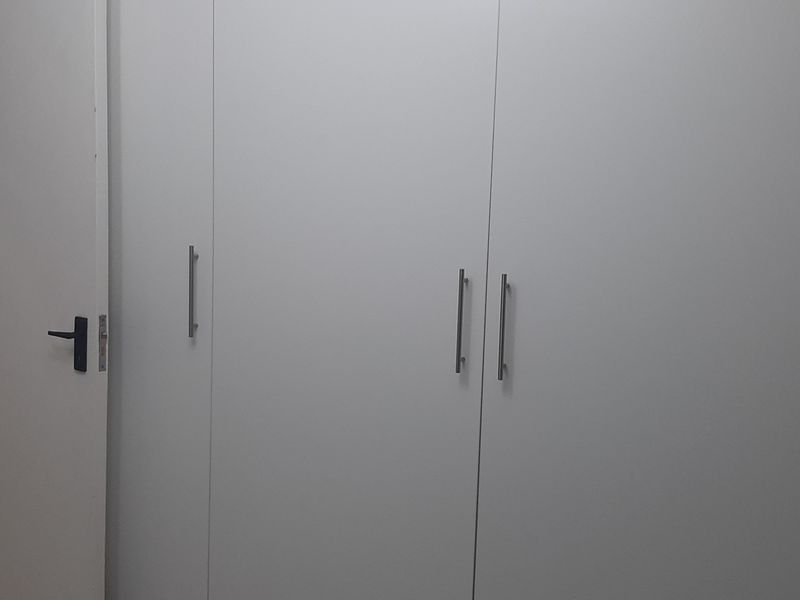 A clean bedroom interior featuring modern white built-in cupboards with sleek metal handles and a neutral tiled floor.